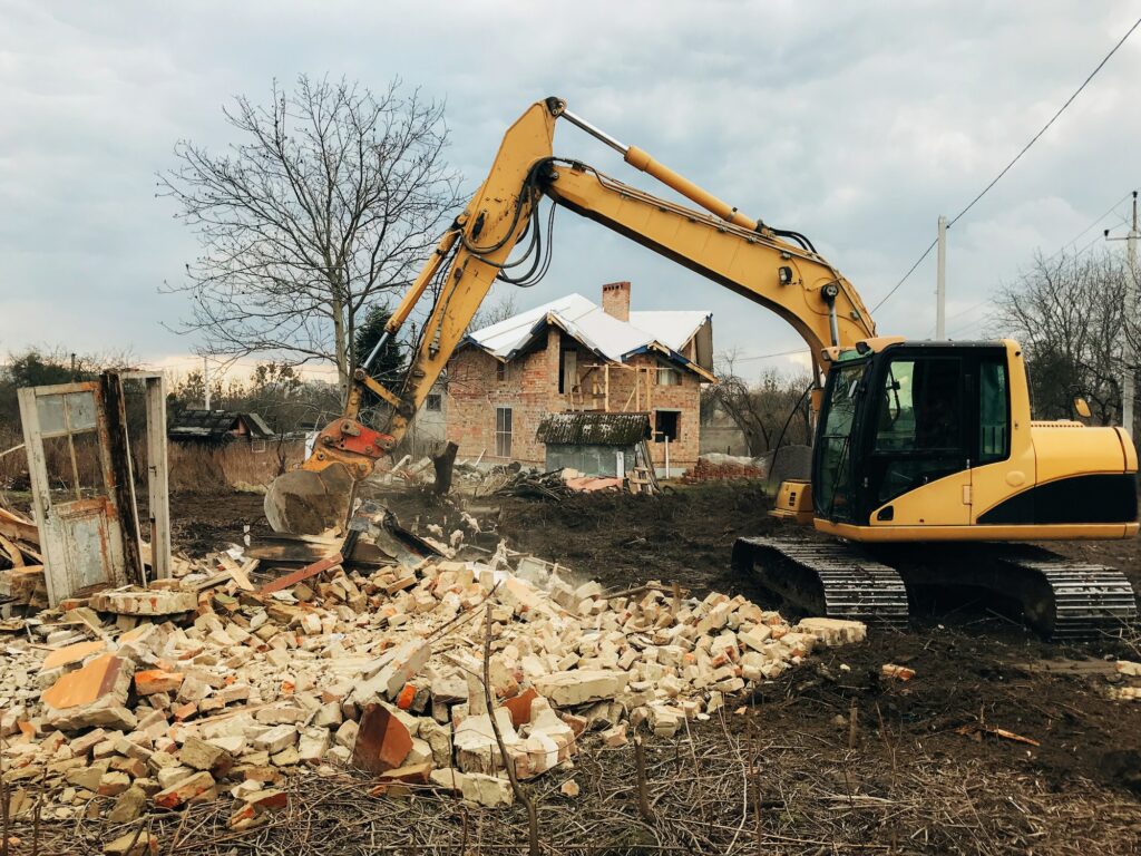 Excavator destroying brick house on land in countryside